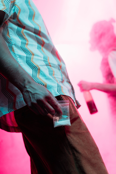partial view of man holding in hand drugs in plastic zipper bag in nightclub - Foto, imagen