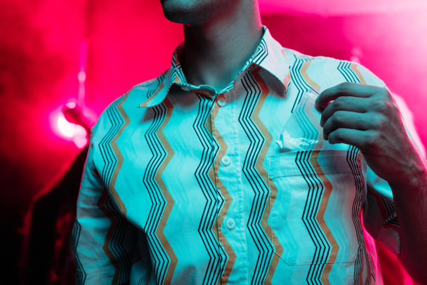 Ausgeschnittener Blick auf Mann, der Drogen in Plastiktüte in Diskothek steckt - Foto, Bild