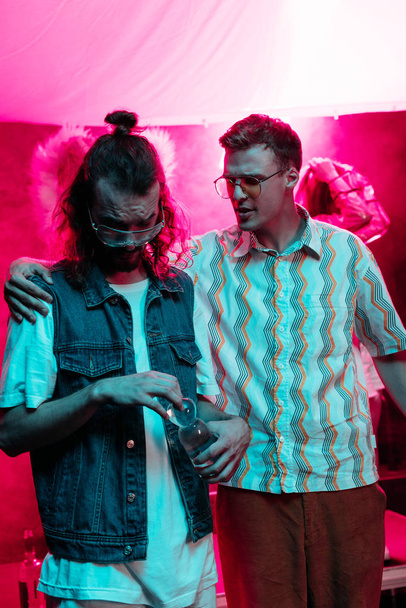 чоловік обіймає іншого чоловіка з пляшкою води в нічному клубі під час вечірки
  - Фото, зображення