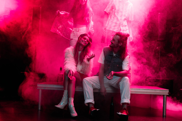 feliz hombre y mujer joven sentados juntos durante fiesta rave en discoteca
 - Foto, Imagen