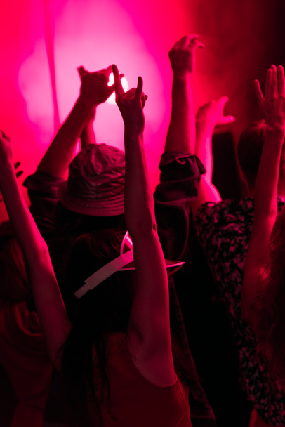 Вид сзади людей с поднятыми руками во время рейв-вечеринки в ночном клубе с розовой подсветкой
 - Фото, изображение