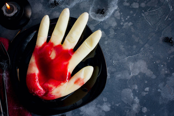 Vanilla pudding in the shape of a hand with cherry sauce on a black Halloween table, top view, horizontal, copy space. - Φωτογραφία, εικόνα