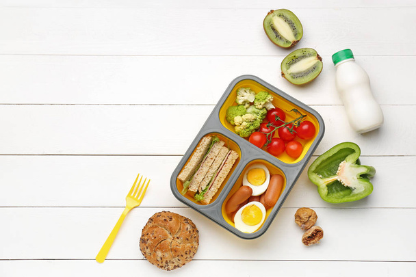 Caixa de almoço com comida saborosa em fundo de madeira branca
 - Foto, Imagem