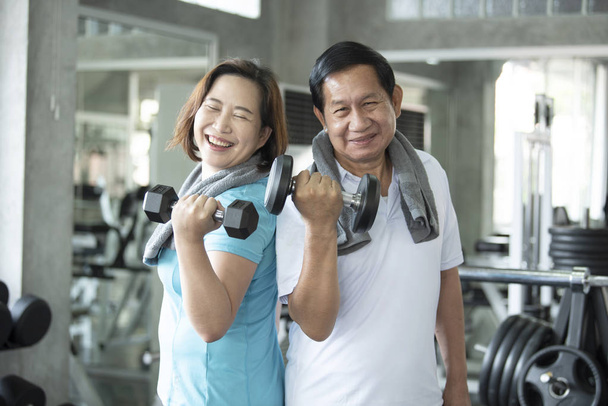 Azjatycki senior mężczyzna i kobieta ćwiczą podnoszenie hantli w siłowni. w podeszłym wieku zdrowy styl życia. - Zdjęcie, obraz