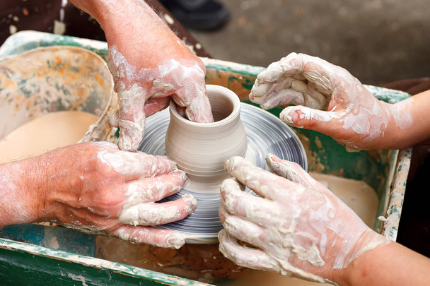 Close-up aardewerk. Volwassen Potter modderige handen begeleiden kind handen om te helpen met klei op een wiel - Foto, afbeelding
