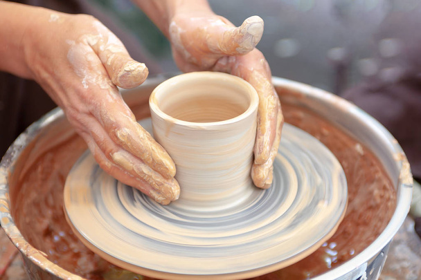 Close up pottery. Adult potter muddy hands guiding child hands to help with clay on a wheel - Photo, Image