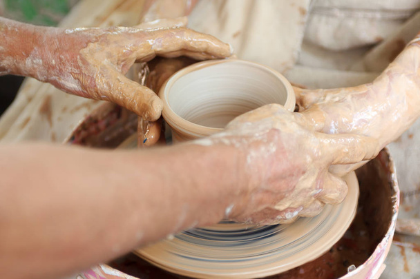 Close up pottery. Selective focus. Adult potter muddy hands guiding students hands to help with clay on a wheel - Foto, Imagen
