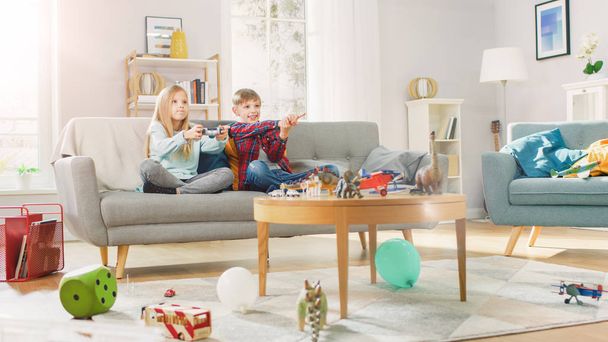 At Home: Cute Girl Playing in Video Game Console, Using Joystick Controller, Her Younger Brothe Cheers for Her. Happy Children Playing Videogames. - 写真・画像