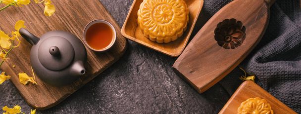 Mid-Autumn Festival traditional food concept - Beautiful Moon cake on black slate table with tea, pastry mold, flower, top view, flat lay, copy space - Фото, зображення
