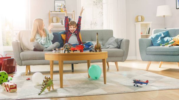 At Home: Smart Boy Playing in Video Game Console, Using Joystick Controller, His Older Sister Sits Near on Sofa and Cheers for Him. They Win and Celebrate Happily. Happy Children Playing Videogames. - Foto, Imagen