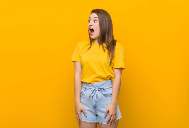 Νεαρή γυναίκα έφηβος φορώντας ένα κίτρινο πουκάμισο σοκαρισμένοι λόγω κάτι που έχει δει. - Φωτογραφία, εικόνα