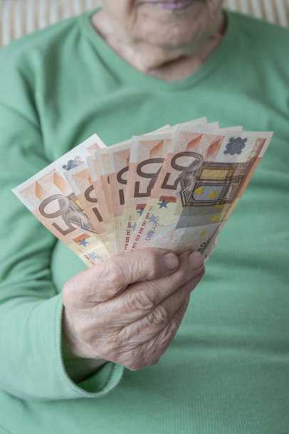 wrinkled hand of a senior woman holding euro banknotes - Foto, afbeelding