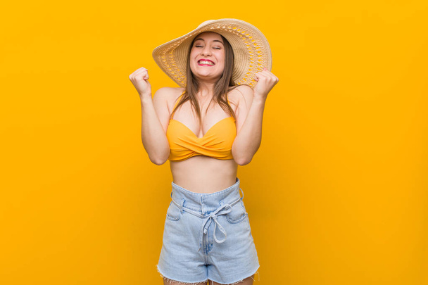 Mujer caucásica joven con un sombrero de paja, mirada de verano levantando el puño, sintiéndose feliz y exitoso. Concepto de victoria
. - Foto, imagen