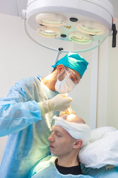 The surgeon gives injections to the head. Baldness treatment. Hair transplant. Surgeons in the operating room carry out hair transplant surgery. Surgical technique that moves hair follicles from a - Fotó, kép