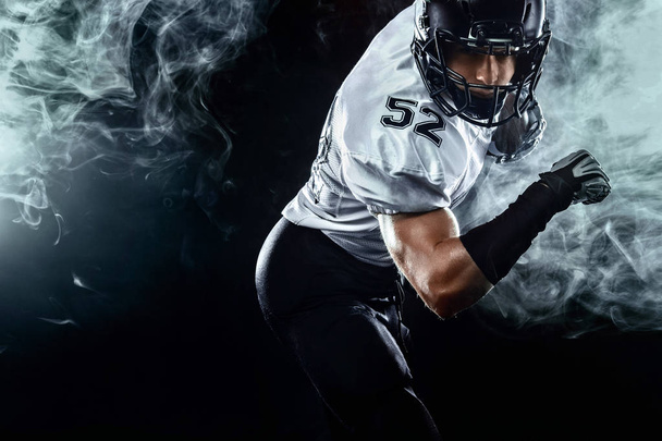 American football sportsman player in helmet on black background with smoke. Sport and motivation wallpaper. - Foto, Imagen