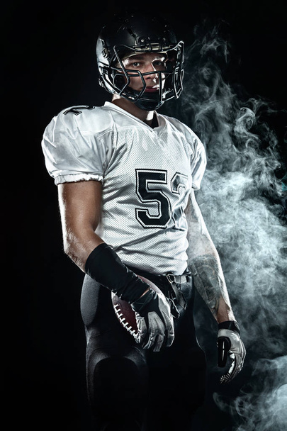 Jugador de fútbol americano deportista en casco sobre fondo negro con humo. Fondo de pantalla deporte y motivación
. - Foto, Imagen