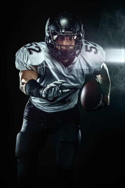 American football player, sportsman in helmet on black background with smoke. Sport and motivation wallpaper. - Foto, Imagen