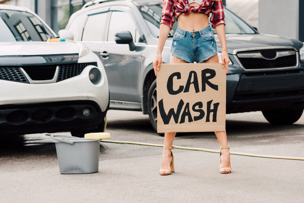 cropped view of girl standing and holding carton placard with car wash letters near cars  - Foto, imagen