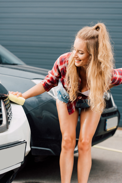 happy woman holding yellow sponge while washing car  - Foto, Bild