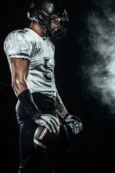 American football sportsman player in helmet on black background with smoke. Sport and motivation wallpaper. - Photo, Image