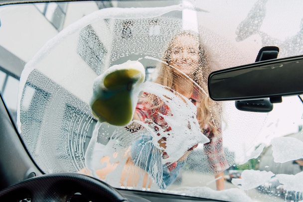 επιλεκτική εστίαση της γυναίκας καθαρισμού αυτοκίνητο με σφουγγάρι και αφρό  - Φωτογραφία, εικόνα