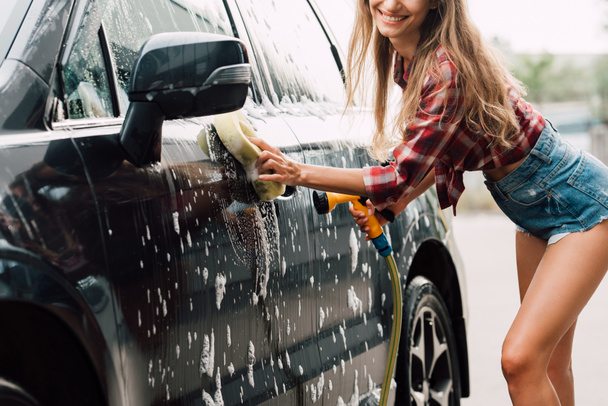 cropped view of positive girl washing wet car in foam  - Фото, изображение
