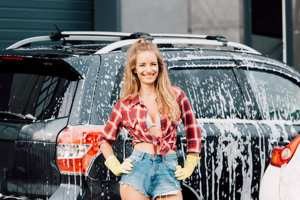 cheerful girl standing with hands on hips near cars  - Фото, зображення