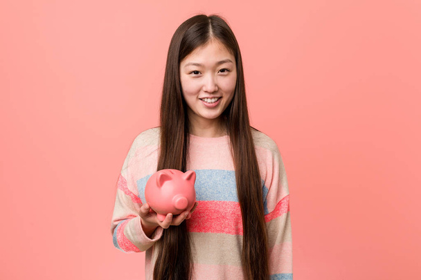 Jeune femme asiatique tenant une tirelire heureux, souriant et joyeux
. - Photo, image