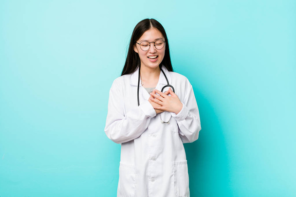 Joven doctora china riendo manteniendo las manos en el corazón, concepto de felicidad
. - Foto, Imagen