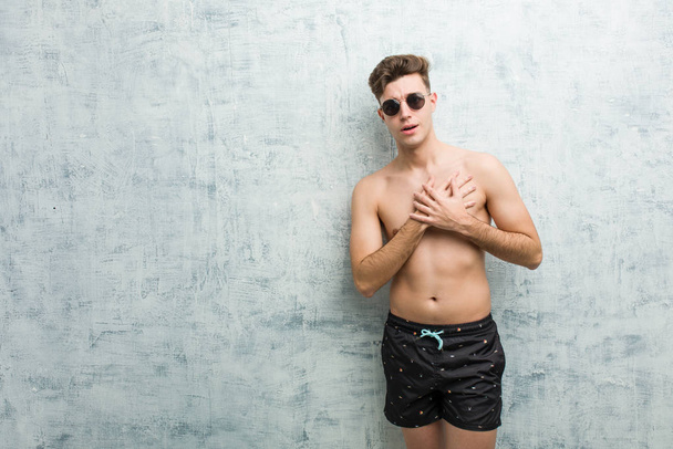 Mladý Kavkazský muž, který nosí plavky, má přátelský výraz, tlačí dlaň na prsa. Milostný koncept. - Fotografie, Obrázek