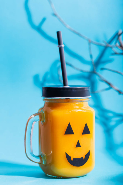 Halloween healthy pumpkin or carrot and tomato drinks in the glass jar with scary face on a blue background - Zdjęcie, obraz