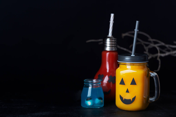 Halloween healthy pumpkin or carrot and tomato drinks in the glass jar with scary face on a dark background - Фото, зображення