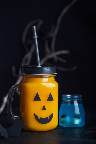 Halloween healthy pumpkin or carrot drink in the glass jar with scary face on a black background - Фото, изображение