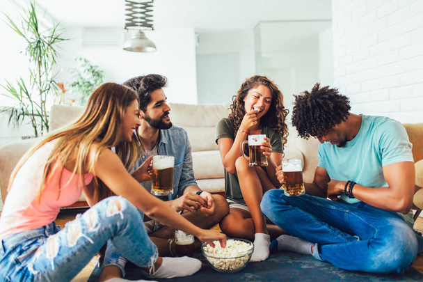 Друзья едят попкорн и пьют пиво кружку дома, весело
 - Фото, изображение