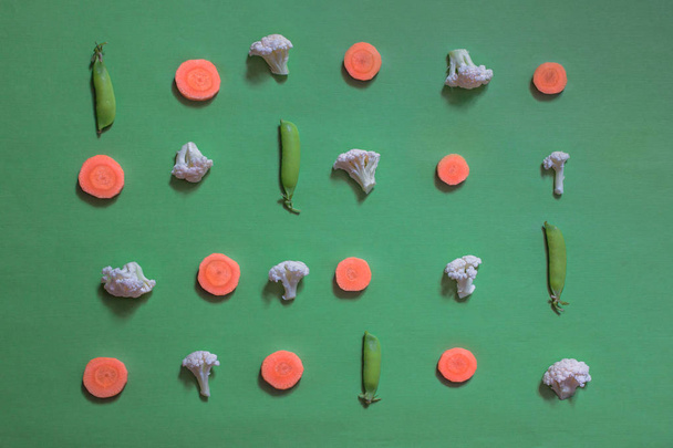 the layout of cauliflower roaches, carrot pieces and pea pods on a green background, the concept of healthy eating, diet, weight loss, vegetarianism - Фото, зображення