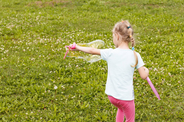 kleines Mädchen, blond, spielt auf der Wiese und pustet eine Blase. - Foto, Bild