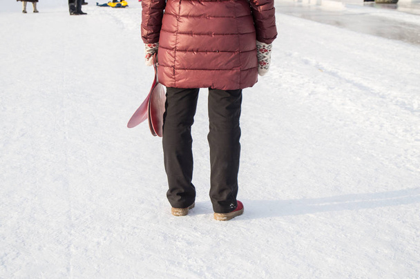 Вид с задней стороны женщины в зимней одежде, стоящей в снегу в парке и держащей сани, лед, ожидающей своих детей
 - Фото, изображение