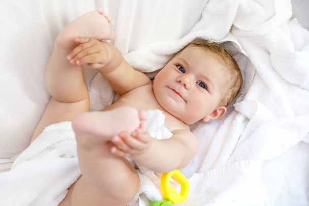 Schattige kleine baby spelen met speelgoed rammelaar en eigen voeten na nemen bad. Schattige mooie meisje verpakt in witte handdoeken - Foto, afbeelding
