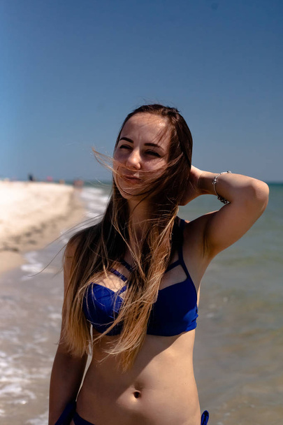 Ένα νεαρό κορίτσι με ένα μαγιό στην παραλία δίπλα στη θάλασσα. - Φωτογραφία, εικόνα
