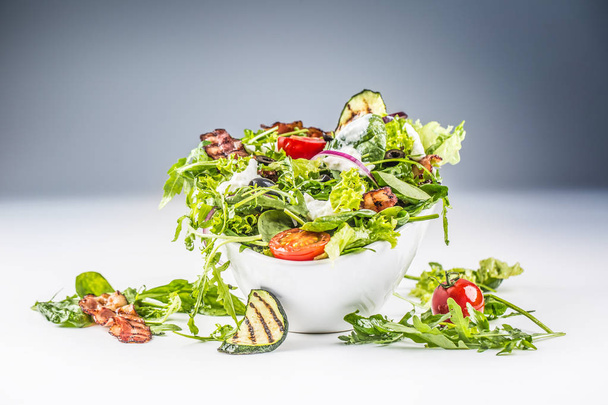 Fresh vegetable salad with fried bacon tomatoes olives arugula zucchini tzatziki dressing and olive oil - Foto, Imagen