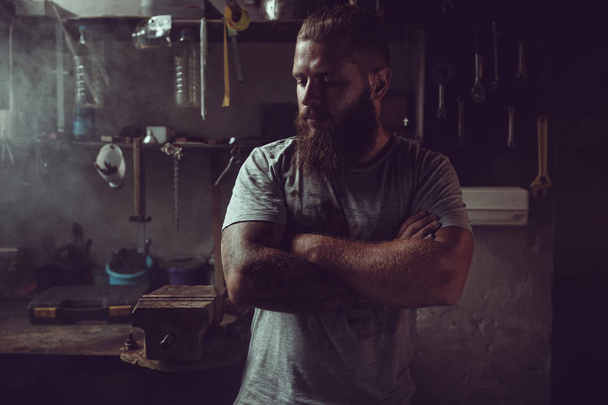 Bel homme brutal avec une barbe debout dans son garage sur fond d'outils de réparation
 - Photo, image