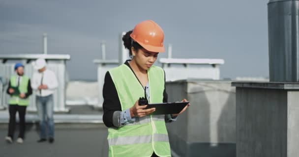 The mixed skin young construction lady looks very focused on her work as she looks astonished at her iPad , she is very gorgeous, and looks cute wearing an orange construction helmet - Imágenes, Vídeo