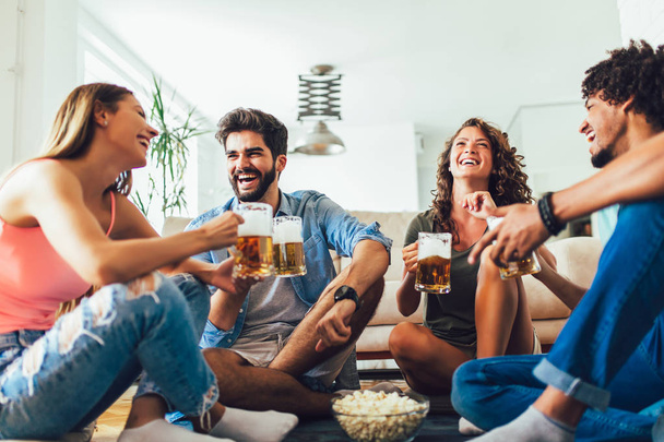 Друзья едят попкорн и пьют пиво кружку дома, весело
 - Фото, изображение