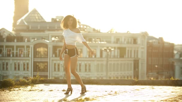 Uma jovem mulher de shorts pequenos que se levanta do chão e executa dança sexy atraente no telhado - pôr do sol brilhante
 - Filmagem, Vídeo