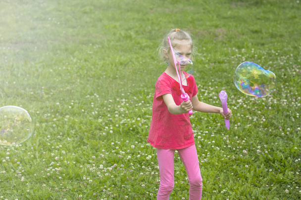 kleines Mädchen, blond, spielt auf der Wiese und pustet eine Blase. - Foto, Bild