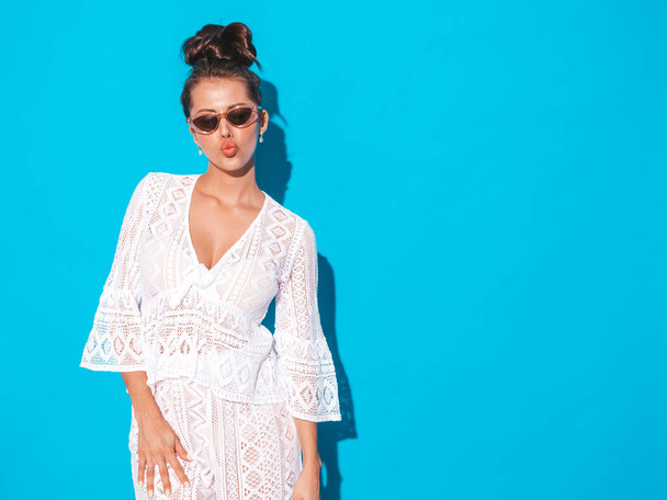 Portrait of young beautiful sexy smiling woman with ghoul hairstyle. Trendy girl in casual summer white hipster suit clothes in sunglasses. Hot model isolated on blue.Makes duck face - Foto, Imagem