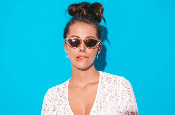Portrait of young beautiful sexy smiling woman with ghoul hairstyle. Trendy girl in casual summer white hipster suit clothes in sunglasses. Hot model isolated on blue.Biting her lip - Valokuva, kuva