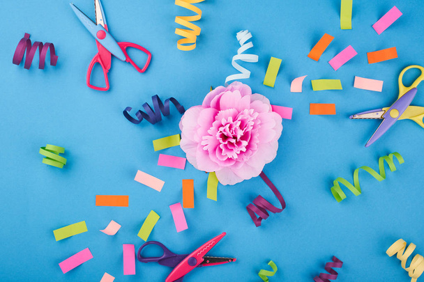 Розовый цветок с цветной бумагой и ножницами на синем фоне
 - Фото, изображение