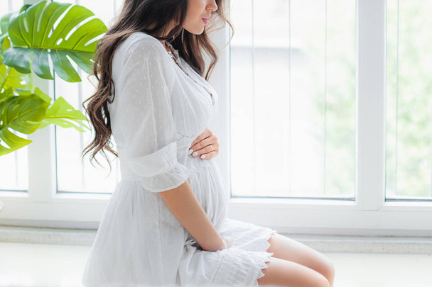 Молода красива вагітна жінка в білій сукні
 - Фото, зображення