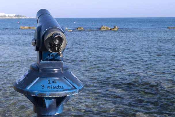 Close-up of a coin operated tourist telescope in front of the Mediterranean sea at the Paphos seaside on a sunny summer day - Fotó, kép